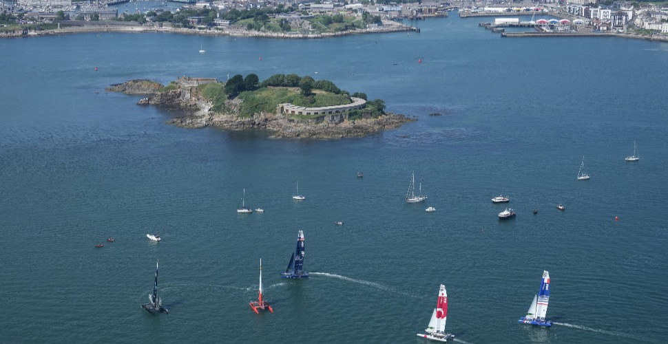SailGP F50 catamarans sailing in Plymouth Sound against a backdrop of Drake's Island and the city in the distance